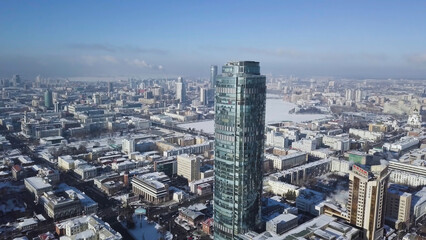 Fototapeta na wymiar Aerial view of skyscraper is in the middle of the city in winter, blue sky sky and snowy roofs of buildings background
