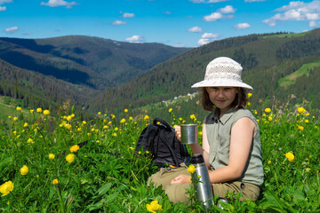 Little cute girl sitting on the top of the mountain, drinking tea from thermos.