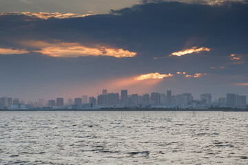 Fototapeta na wymiar 舞浜海岸から見た雲の合間からビル群に射し込む夕陽の光