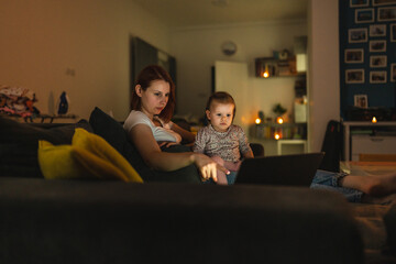Small caucasian child little girl toddler mother and daughter sitting in dark room at night at home on sofa bed watching cartoons or movies on laptop computer real people family growing up copy space