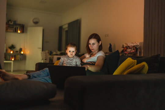 Small Caucasian Child Little Girl Toddler Mother And Daughter Sitting In Dark Room At Night At Home On Sofa Bed Watching Cartoons Or Movies On Laptop Computer Real People Family Growing Up Copy Space