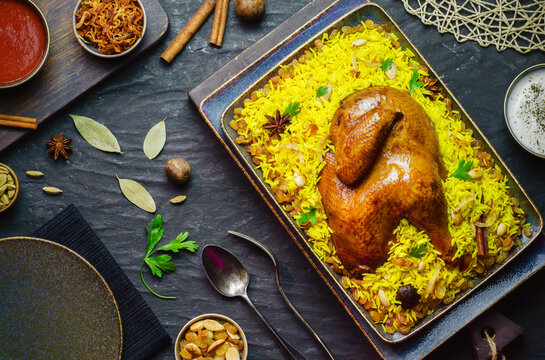 Arabic cuisine; Chicken "Kabsa" or Chicken Beryani rice. Served with golden fried onions, crispy roasted nuts and raisin, fresh parsley, tomato and yogurt sauce. Close up with copy space.