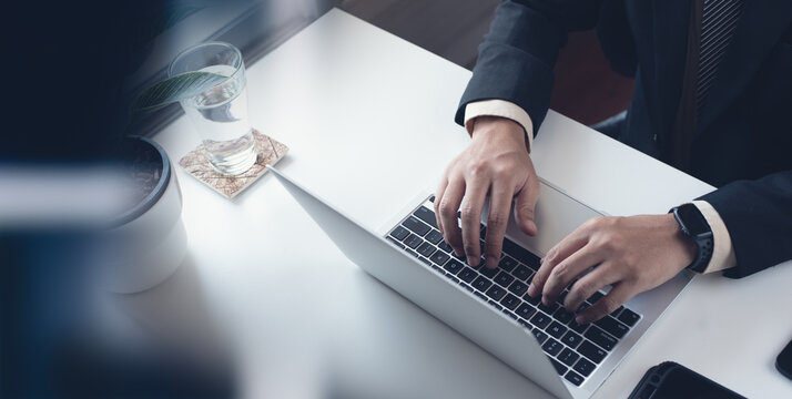 Business Man Working On Laptop Computer At Modern Office. Businessman In Black Suit Working And Typing On Laptop Keyboard, Surfing The Internet With Digital Tablet On Office Table