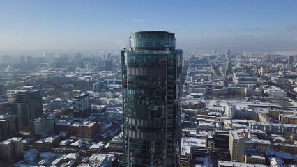 Aerial view of skyscraper is in the middle of the city in winter, blue sky sky and snowy roofs of buildings background