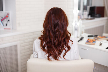 Female back with long, curly, red hair, in hairdressing salon
