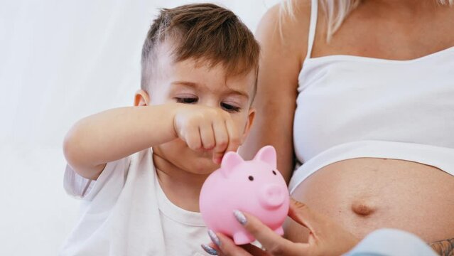 Little caucasian boy focused on carefully putting coins into his piggy bank. Responsible mother learning her child how to save money. High quality 4k footage