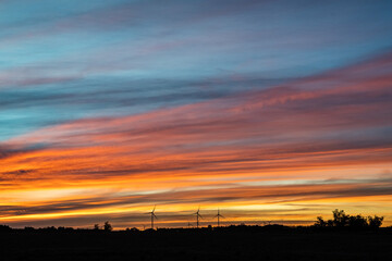 The silhouette of multiple modern windmills on the low horizon in a colorful sunset, outside of Kiyú, San José, Uruguay