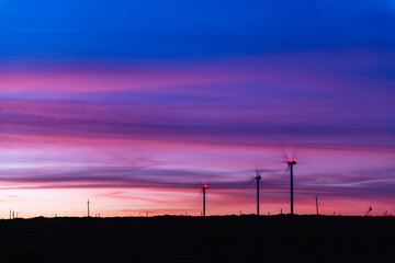 The silhouette of multiple modern windmills on the low horizon in a colorful sunset, outside of Kiyú, San José, Uruguay