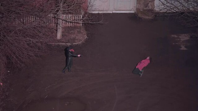 Zombie raised its arms and hobbled to attack human. Person in hat and plague doctor mask shoots a monster and it falls dead on the ground, a view from a height