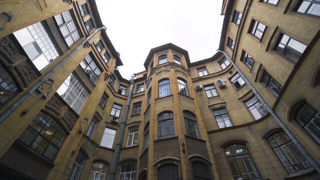 Courtyard of old round building in city. Action. Bottom view of old house with courtyard well on background of sky. Old closed courtyards of houses in St. Petersburg - Powered by Adobe