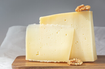 Pair of pieces of hard cheese with walnuts on a gray background