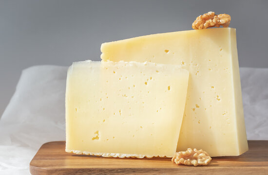 Pair of pieces of hard cheese with walnuts on a gray background