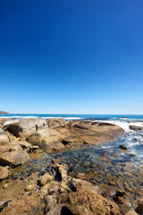 Fototapeta na wymiar Big rocks in the ocean or sea water with a blue sky background. Beautiful landscape with a scenic view of the beach with boulders on a summer day. Relaxing scenery of the seaside or nature