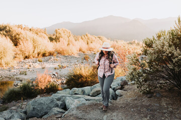 Naklejka premium Young latin woman with a hat and a backpack on, hiking in a beautiful landscape.
