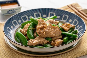 Stir fried chicken breast slices with sugar snap peas, a simple Thai Chinese dish, served on a deep blue plate with a small cup of garlic chili relish.