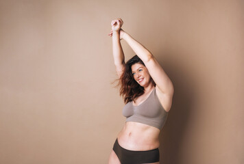 Self loving woman plus size in underwear dancing on beige background, body love