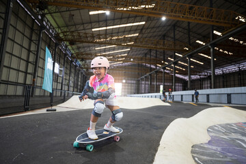asian child or kid girl fun playing skateboard or ride surf skate in indoor pump track in skate park by extreme sports to wearing helmet elbow pads wrist and knee support for body safety on summer © kornnphoto