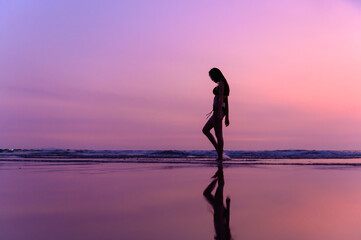 Silhouettte photo of young beautiful Asian woman with bikini walking along beautiful beach at twilight sunset time. Happy or Freedom woman concept.