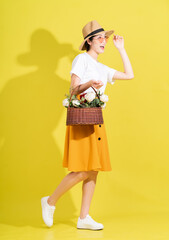 Full length photo of young Asian woman holding flower on yellow background