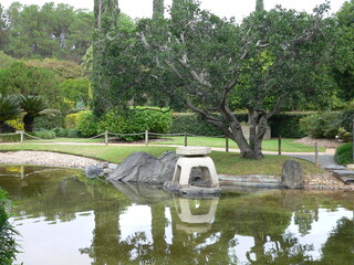 A pond with a sculpture, trees and plants in a garden