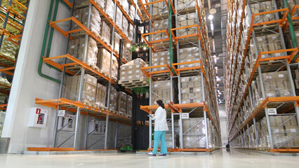 Large modern warehouse with forklifts. Warehouse worker taking package in the shelf in a large warehouse in a large warehouse. storehouse worker sealing cardboard boxes for shipping in storehouse.