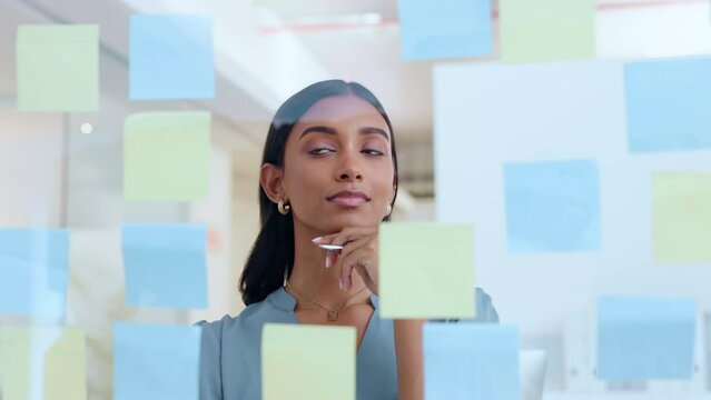 Young female notes on glass wall. Woman brainstorming, planning in a corporate setting showing leadership, management skills in the workplace. Business lady project strategy in office environment.