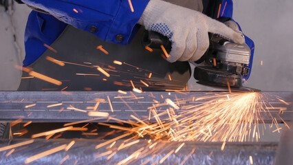 Craftsman sawing metal with disk grinder in workshop. Grinding metal with sparks flying. Electric...