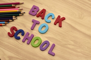 the phrase back to school is laid out in multicolored letters on the table next to colored pencils the concept of education school