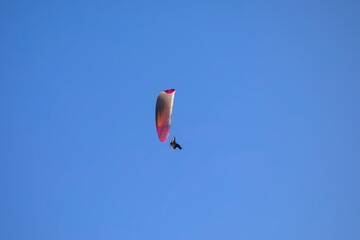 Paraglider in orange and pink colors with motor in front of a blue sky flying in the morning sun