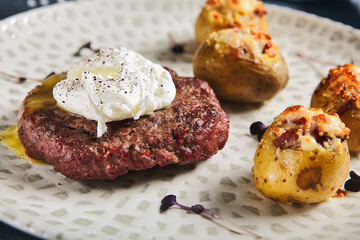 American breakfast - beefsteak with egg and roasted baby potatoes. Beef cutlet with poached egg in and potatoes in plate on stone background. Egg yolk on beef steak. Main course on meat.