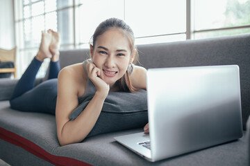 Obraz premium Young Asian woman using laptop computer checking social media application on website online at home, feel relax and enjoy communicate and discuss in living room.