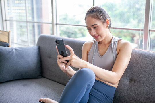 Young Asian woman using smratphone checking social media application on website online at home, feel relax and enjoy communicate and discuss  in living room.