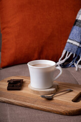 Autumn mood composition with cup of cocoa and chocolate, plaid and books on sofa background. Hot drink in autumn concept