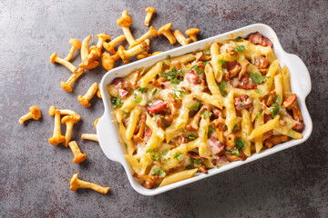 Chanterelle pasta casserole with bacon and cheese served hot from the oven on the table. Horizontal top view from above © FomaA