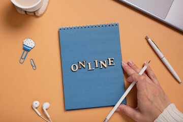 Online text from wooden letters on notepad on desktop with female hand, laptop and coffee cup