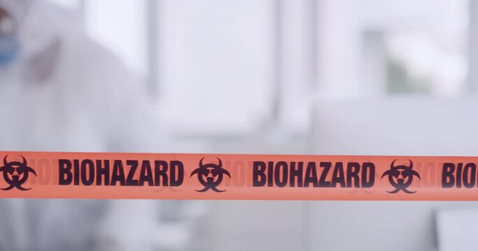 Orange biohazard barrier tape blocking and barricading a secured office space as a caution for disinfection of covid. Team of workers in protective coveralls sanitizing and cleaning a prohibited area