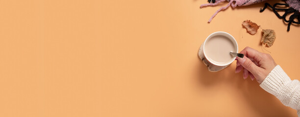 Female hand in sweater holding cup of cocoa on colored background, top view. Banner format with copy space.