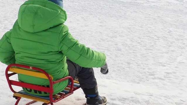 boy sledding in winter. in a green down jacket. walks on the street in winter in snowy weather. happy childhood, winter holidays weekend. sledding down the mountain, throwing snow
