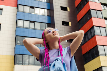 Portrait of a caucasian teenage girl with pink braids against the background of urban high-rise...