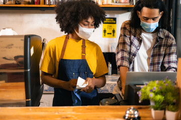 African American young woman waitress in apron and medical looking to camera with open at cafe entrance . Female barrista standing at front counter bar with board open Reopen  During Health Pandemic.
