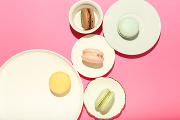 colorful macaroons on white plates on a pink background. top view