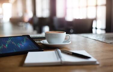 Close up view, tablet computer with graph on screen and white coffee cup on wooden table with note...
