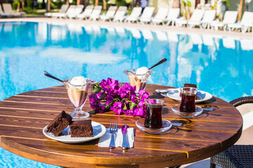 Still life with a glass of tea, brownie, ice cream and a flower on the table beside a swimming pool. Holiday, vacation concept