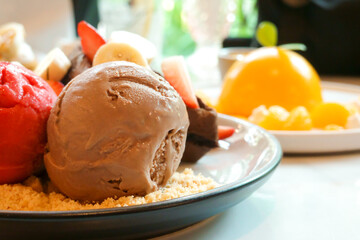 Homemade chocolate and strawberry ice cream with sliced banana on the waffle crumble menu and orange cake behind in a dessert cafe