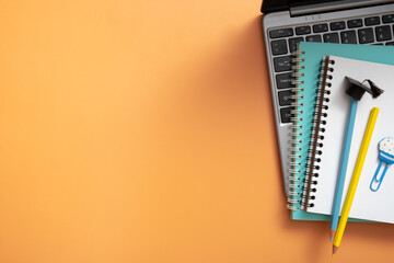 Colorful pencils with graduated cap and note on laptop on colored background. Copy space. Children work space top view, flat lay