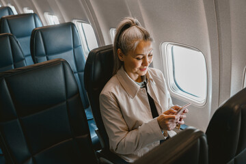 Beautiful Asian woman passenger sitting in the airplane and use phone during boarding