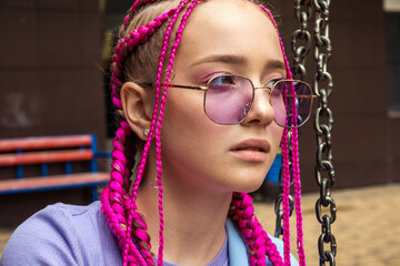 Portrait of a caucasian teenage girl with pink braids swinging on a swing in a city yard.Summer...
