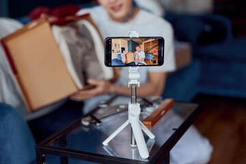 Asian guy making video online at home while using phone on tripod