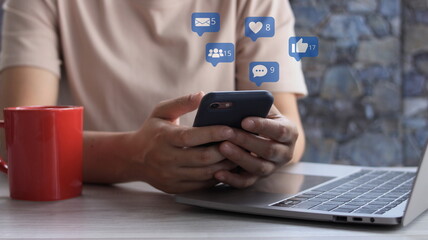 Social media interactions on mobile phone, concept with notification icons of like, message, email, comment  star above smartphone screen.Close up hands using mobile phone internet digital marketing