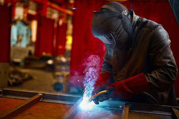 Fototapeta Laborer in protective mask welds manually metal frame obraz